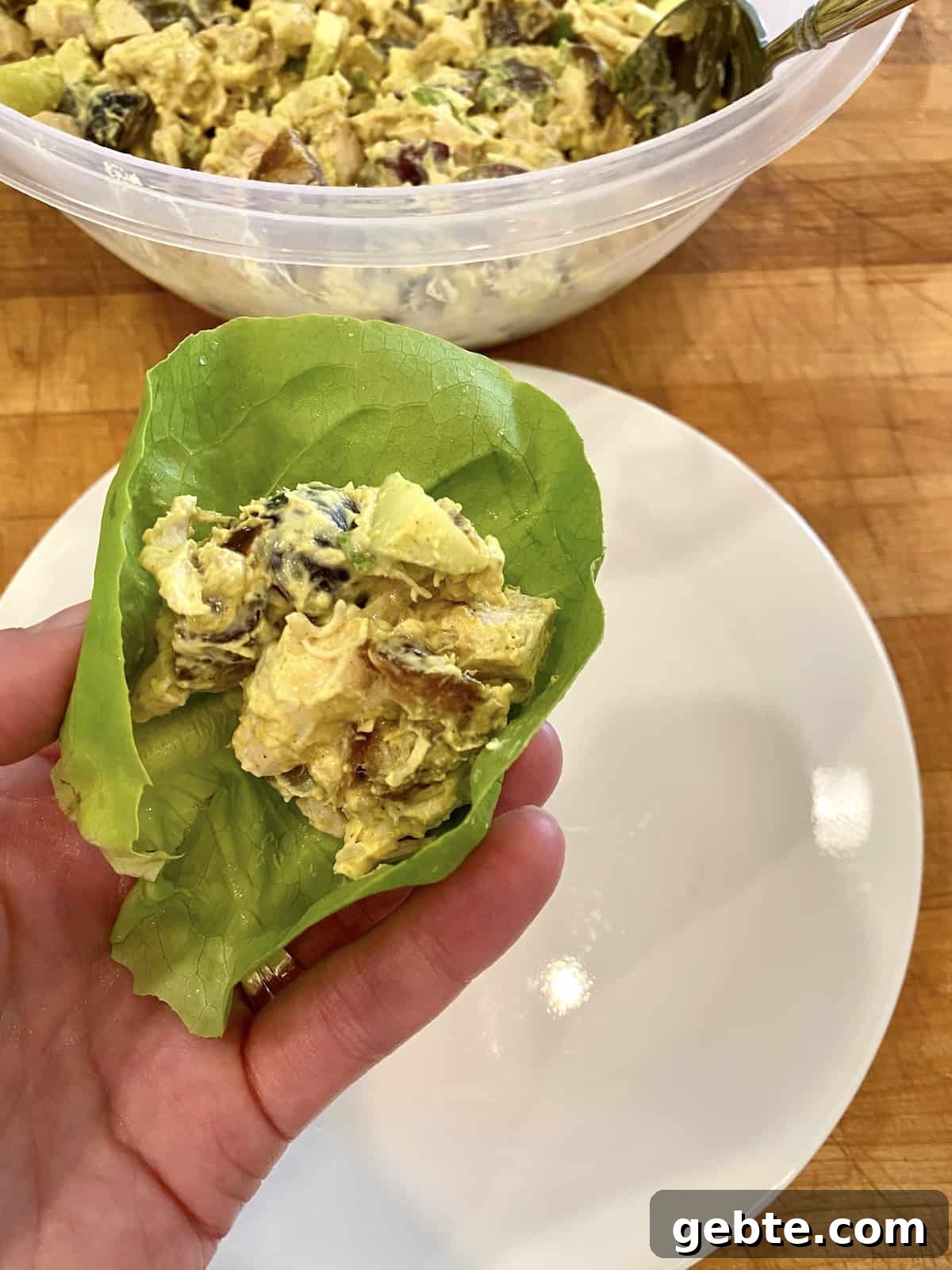 Chicken curry on a lettuce wrap, being held over a plate. 