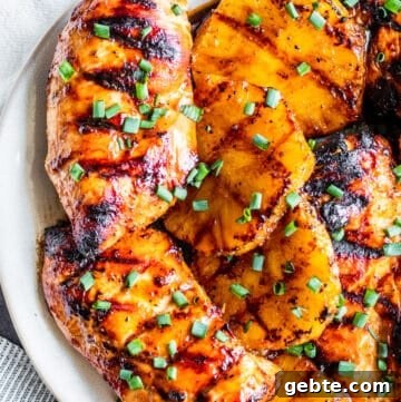 Overhead shot of pineapple chicken with slices of pineapple on white plate.