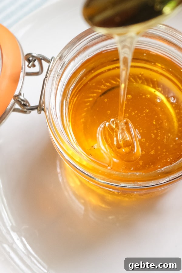 Spoonful of golden syrup drizzling down on a glass jar