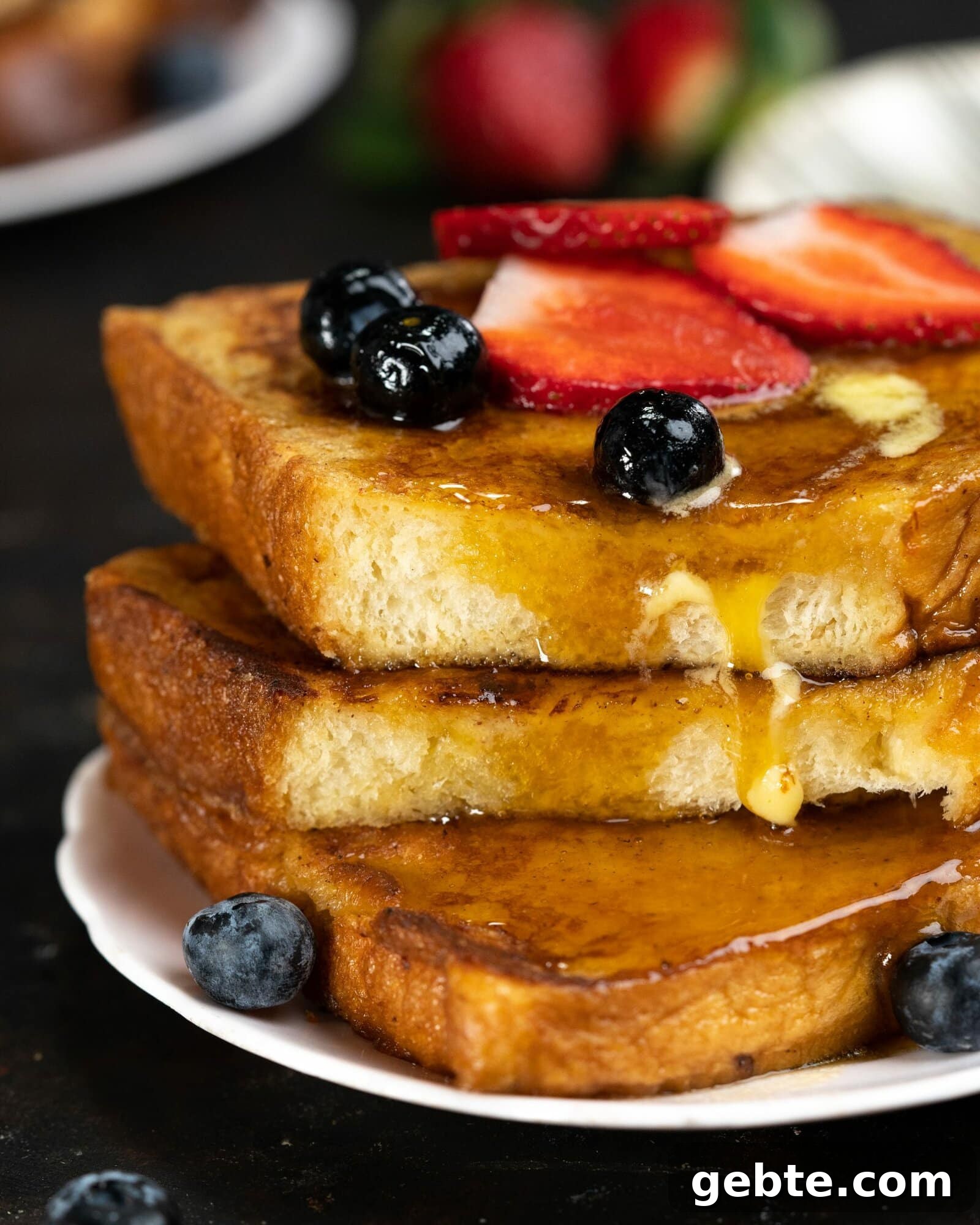 maple syrup dripping down the sides of a stack of brioche bread toasts. it is adorned with berries.