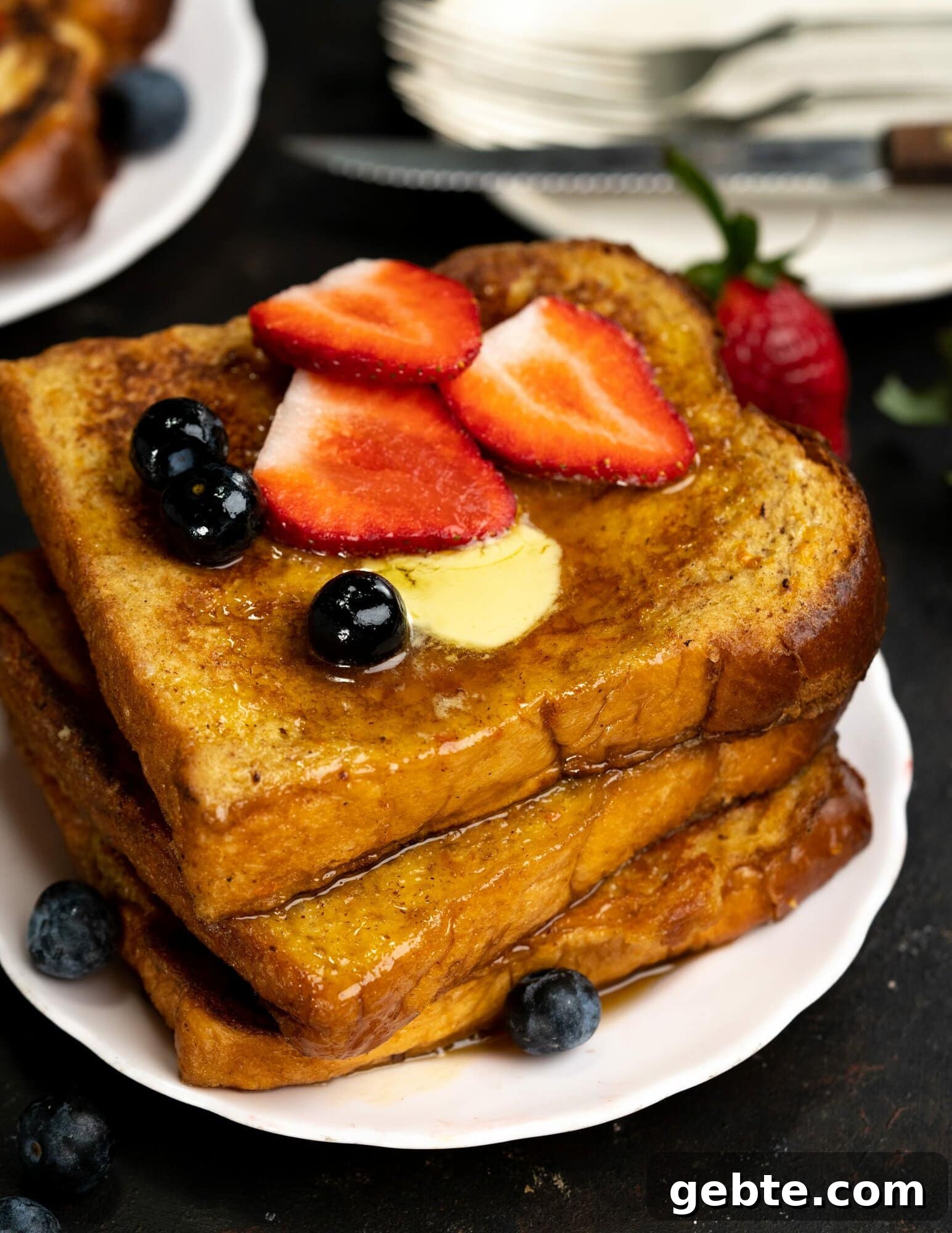 Top view of a stack of brioche toasts which is topped with maple syrup. butter, blueberries and slices of strawberry