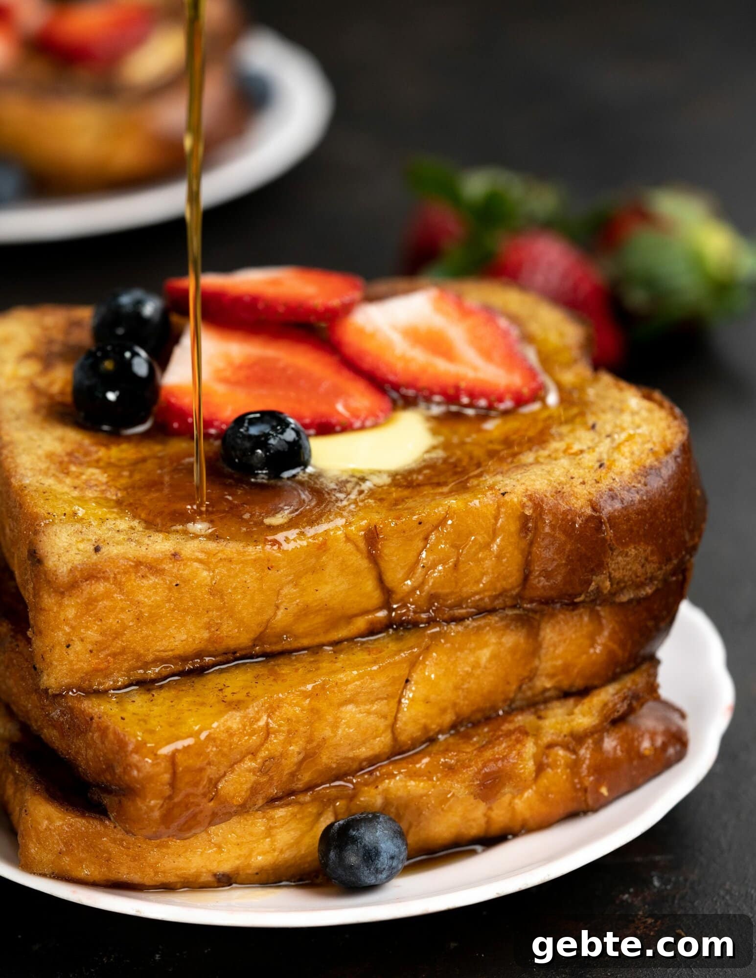 Maple syrup drizzled on a stack of brioche bread toasts, also topped with a dollop of butter and berries.