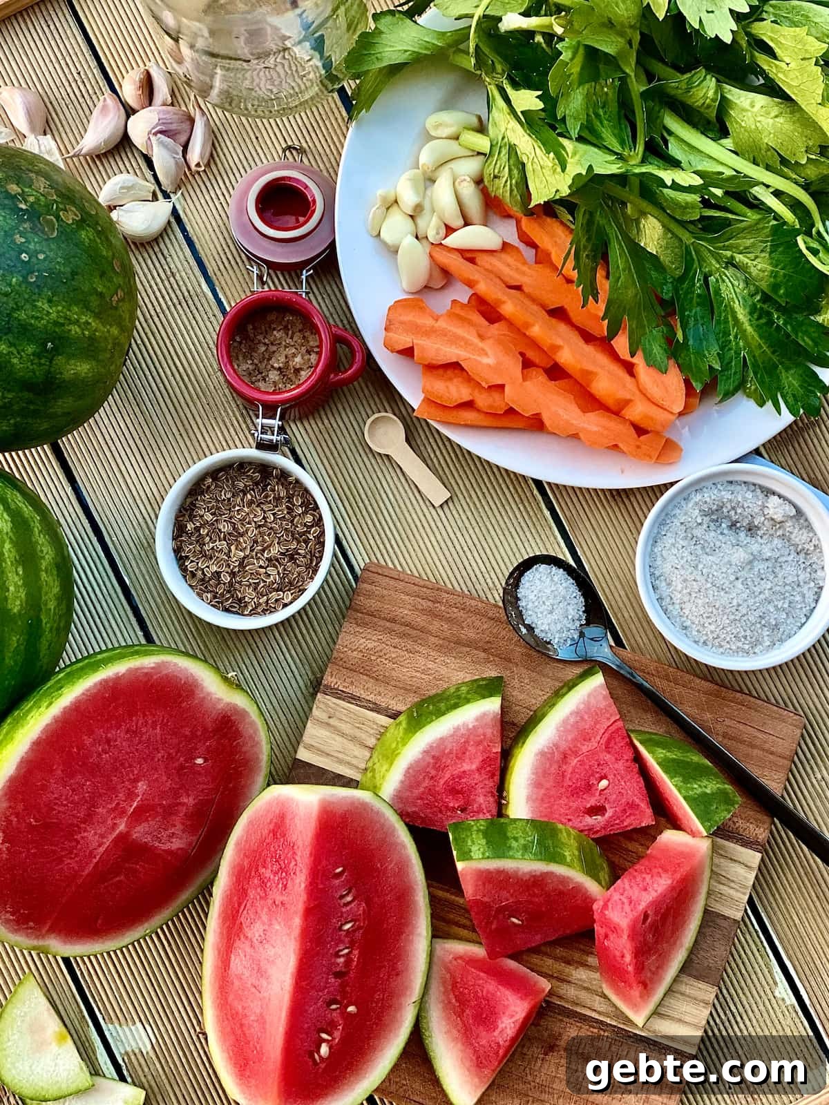 Tangy Pickled Watermelon Rind Recipe for Summer Snacks 3 Fresh watermelon sliced and quartered for pickling, salt in a tiny dish, dill seeds and carrot, garlic cloves, celery leaves, on a white plate