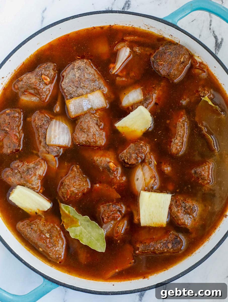 Hearty Oven-Braised Beef Stew Recipe for Comforting Dinners 8 Top down view of beef, tomato broth and onions in a dutch oven.