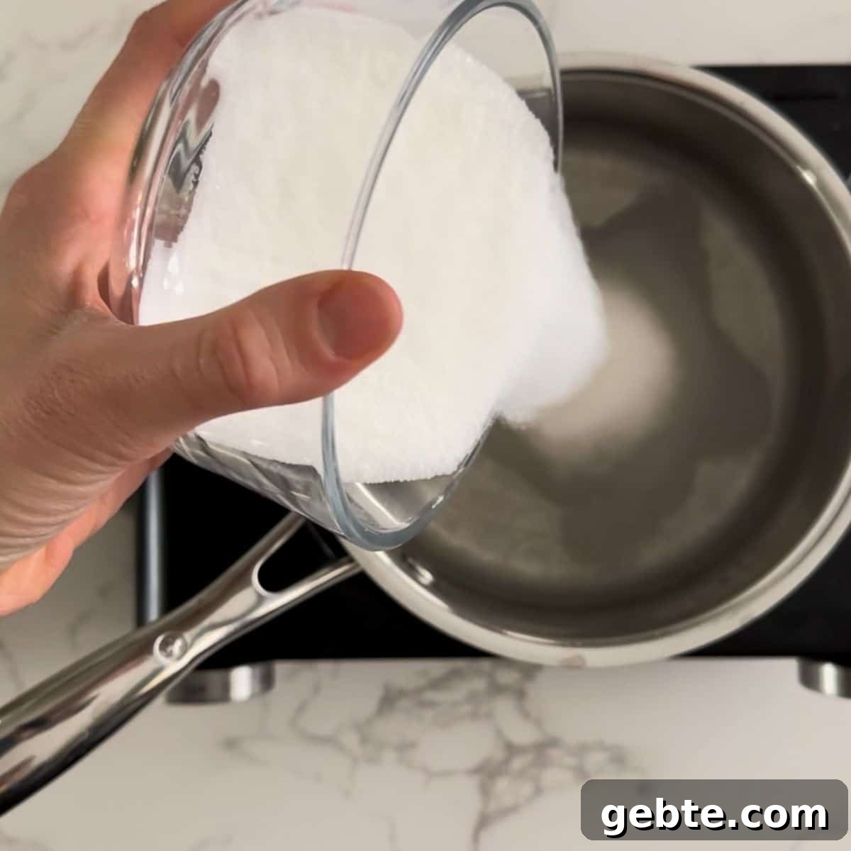 Sugar being poured into a pan of water.