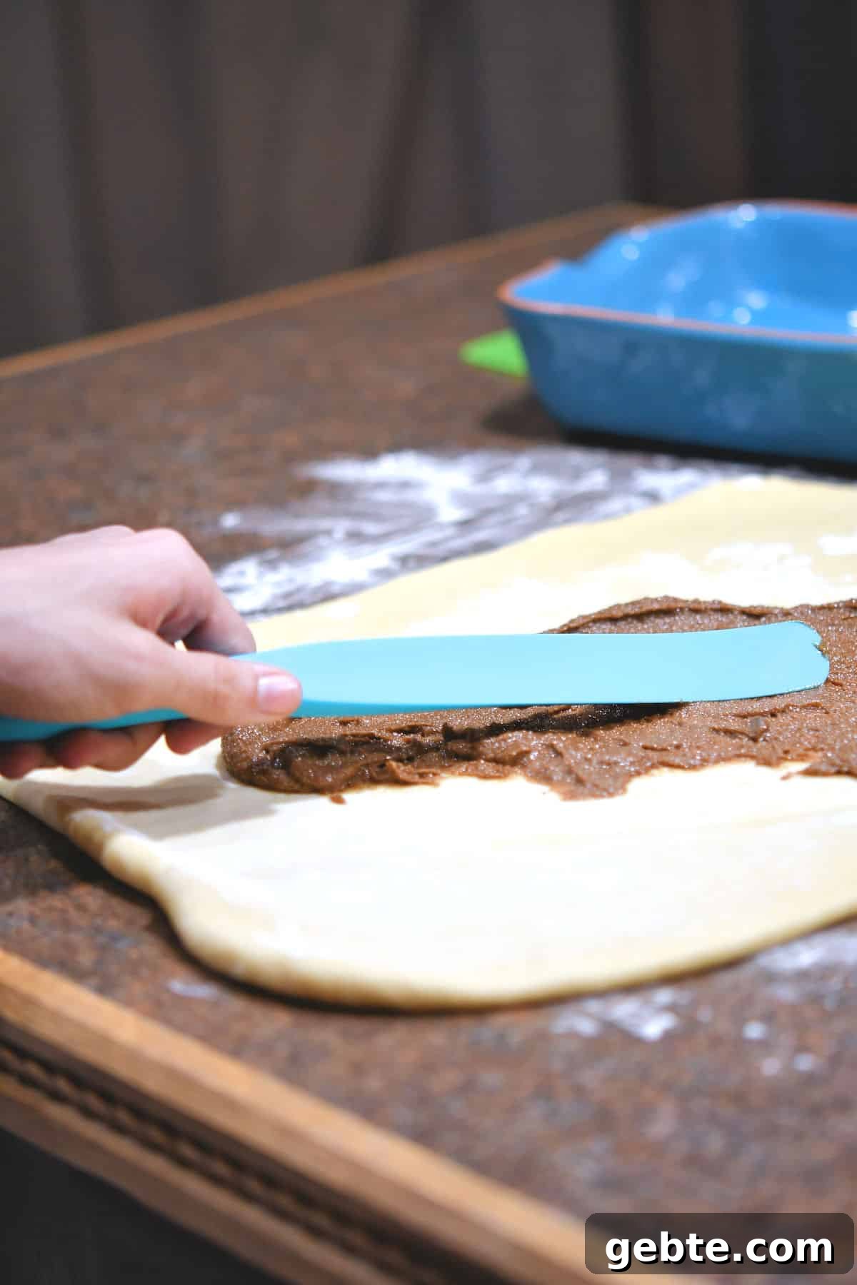 using a spurtle to spread cinnamon mixture on rolled out dough