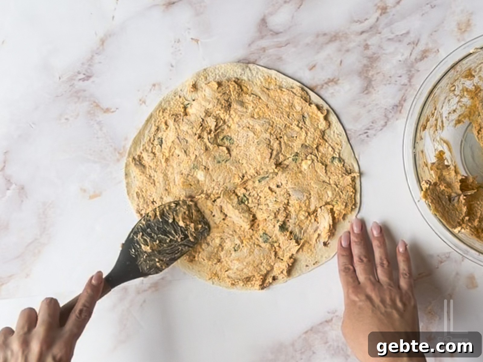 spreading buffalo cream cheese mixture onto a large tortilla.