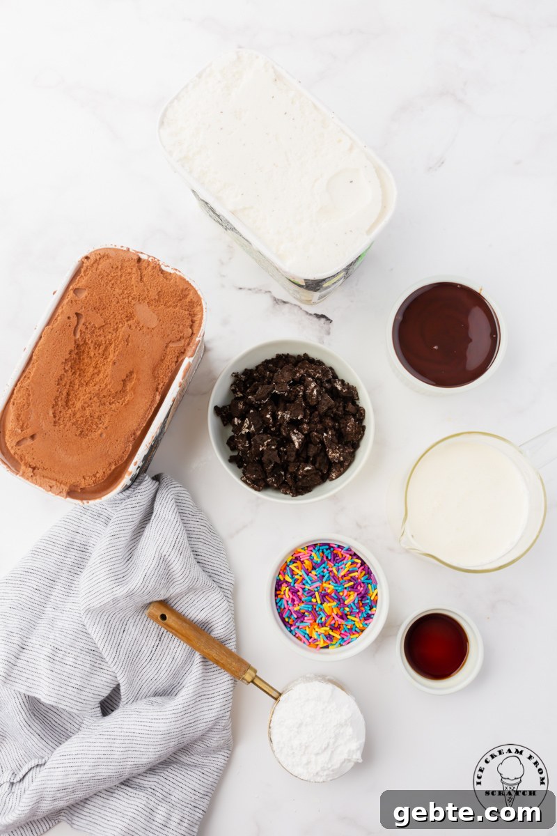 Ingredients for making a classic ice cream cake in separate bowls on a marble countertop. Includes both chocoalte and vanilla ice cream, crushed oreos, fudge sauce, and sprinkles.