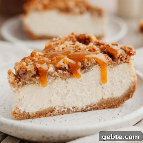 A slice of apple crisp cheesecake drizzled in caramel sauce on a small beige plate.