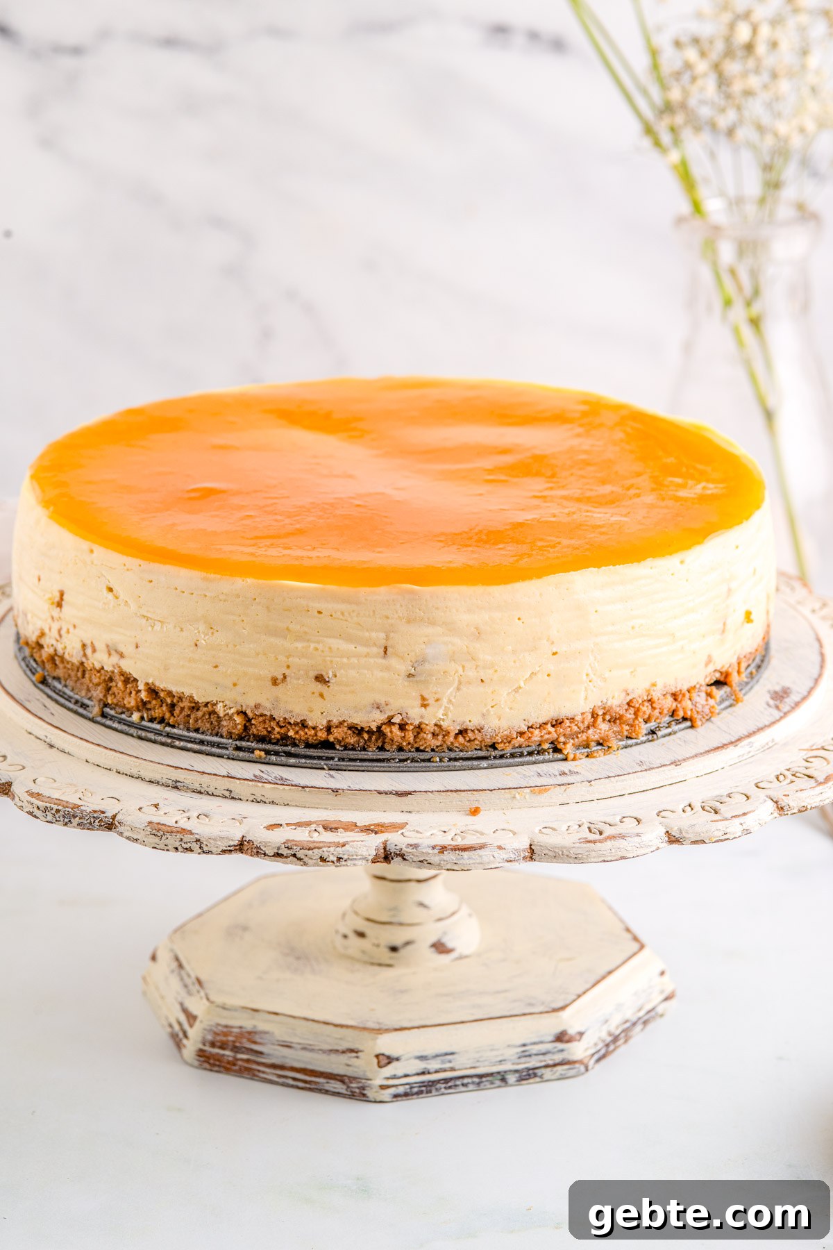 Creamy Peach Cheesecake Recipe with Fresh Peach Topping 10 The finished cheesecake on a cake pedestal.