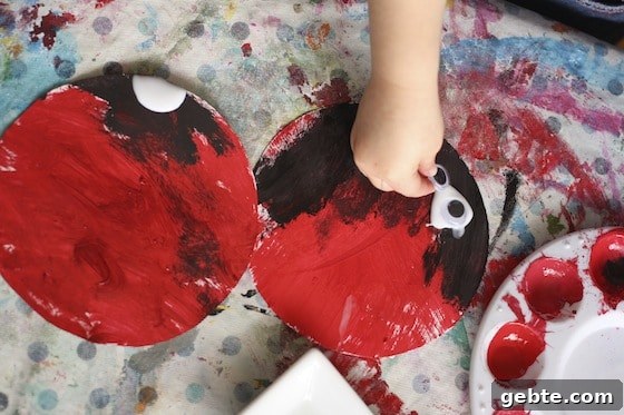 adding black paint and googly eyes to red paper plate