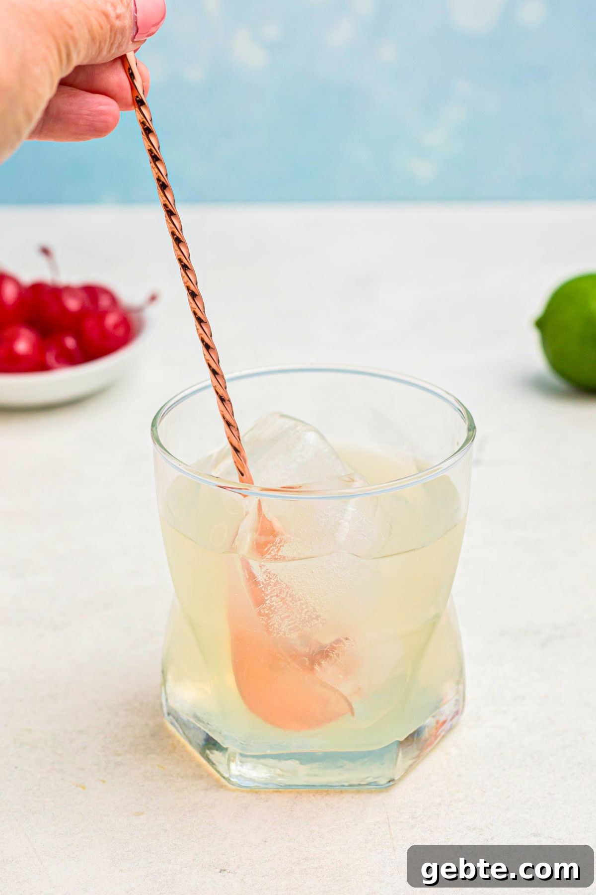 How to Make a Classic Mai Tai Cocktail at Home 5 Ingredients in a clear glass are being stirred together with a rose gold spoon.