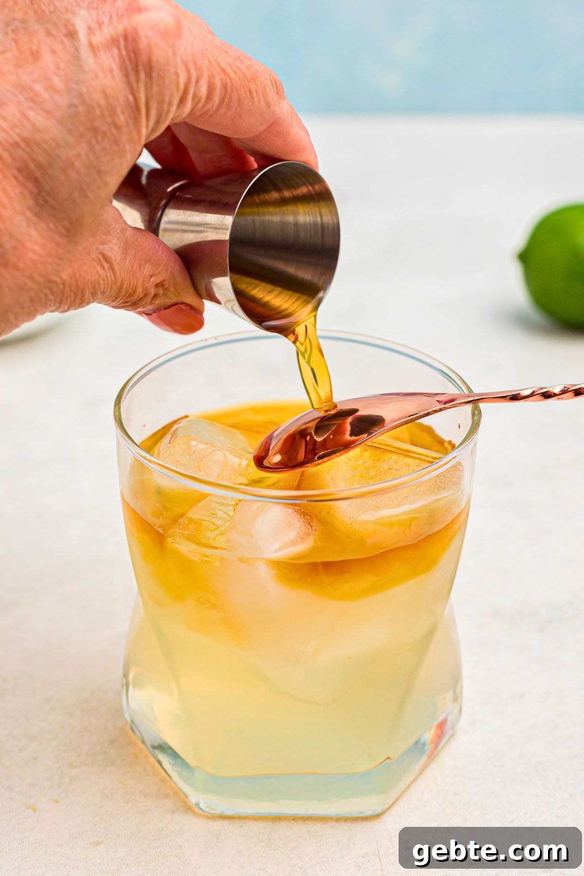 How to Make a Classic Mai Tai Cocktail at Home 6 Dark rum being poured over the back of a spoon to create a layer effect in a mai tai, in a clear glass.