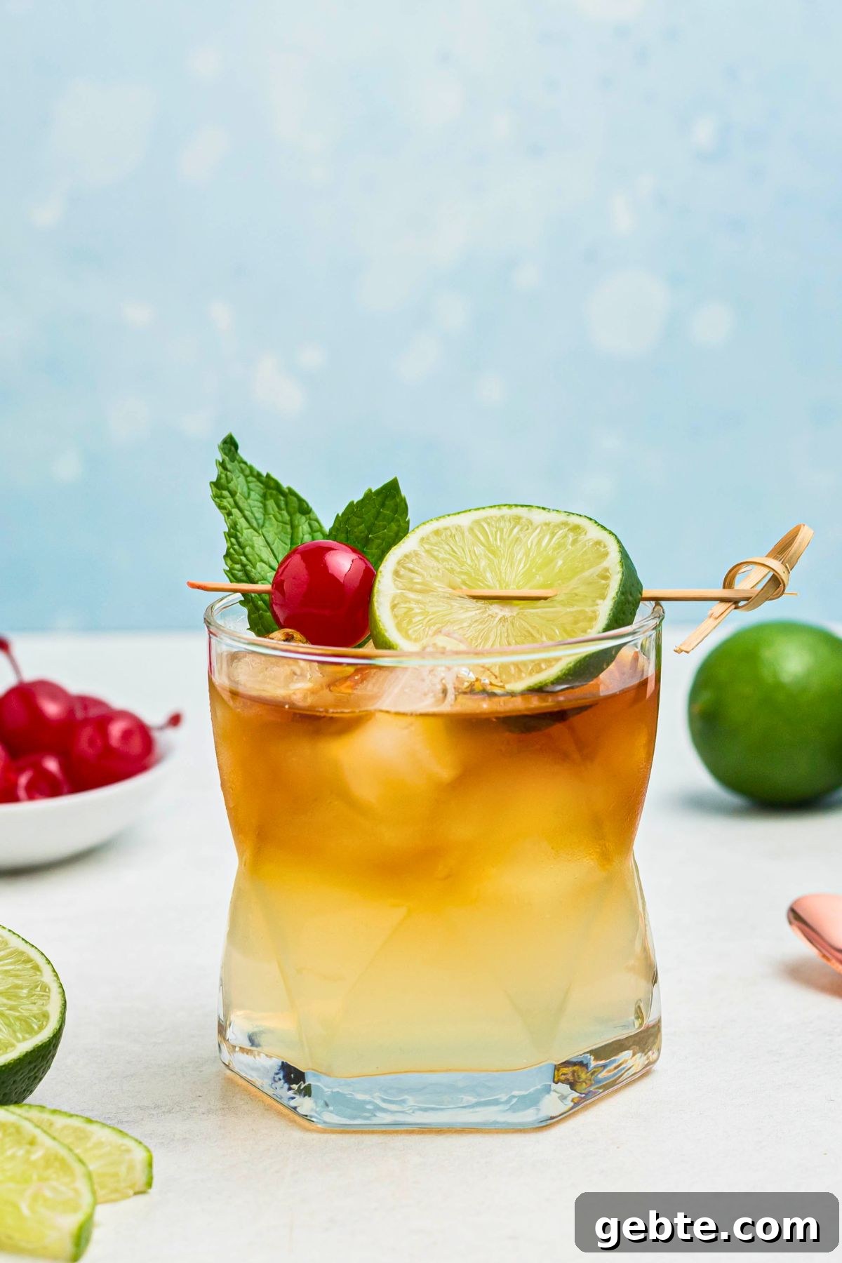 How to Make a Classic Mai Tai Cocktail at Home 7 Rum and other ingredients, mixed together to make a Mai Tai, in a clear half glass, topped with a cherry and lime slice as a garnish.
