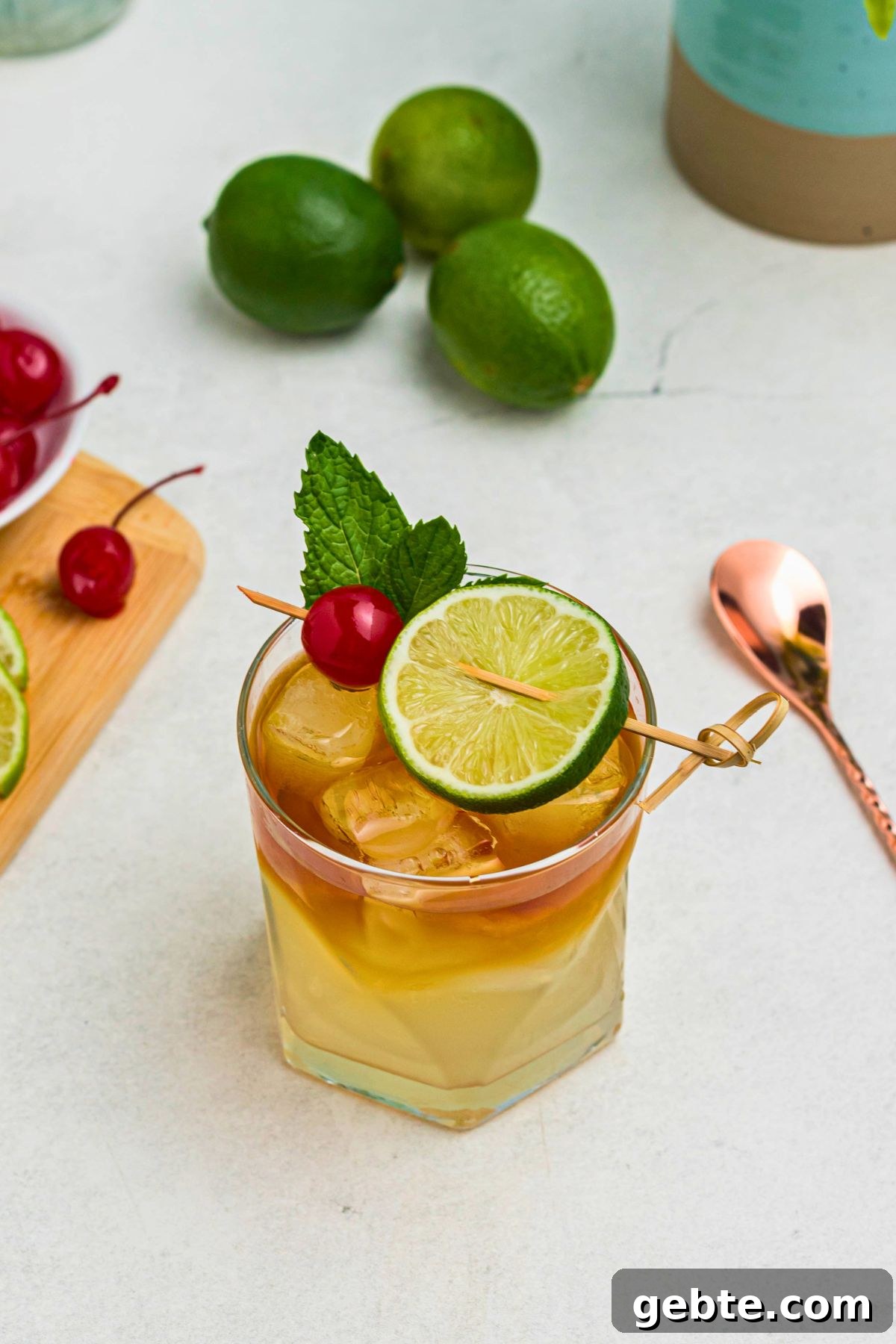 How to Make a Classic Mai Tai Cocktail at Home 8 Overhead image of rum and other ingredients, mixed together to make a Mai Tai, in a clear half glass, topped with a cherry and lime slice as a garnish.