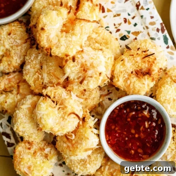 A platter of golden-brown coconut shrimp arranged around two small bowls of red dipping sauce.