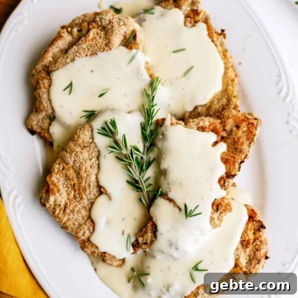 Cube steaks topped with creamy white gravy, garnished with fresh rosemary, served on a white oval plate with a yellow napkin beside it.