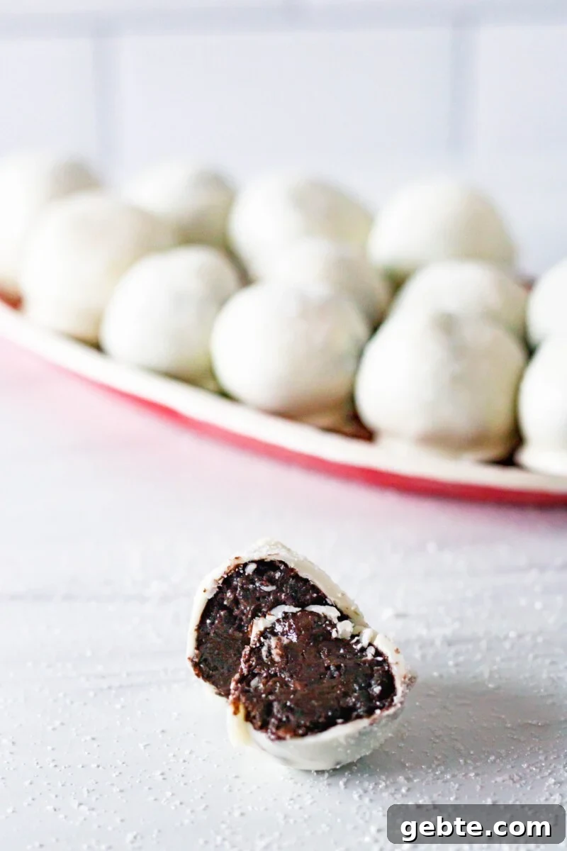 Cut sparkling chocolate cookie truffle on a white surface in front of a tray of more cookie truffles