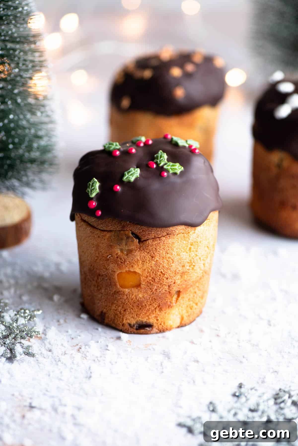 A mini Panettone dipped in melted chocolate sitting on a snowy Christmas themed surface with Christmas trees at the side.