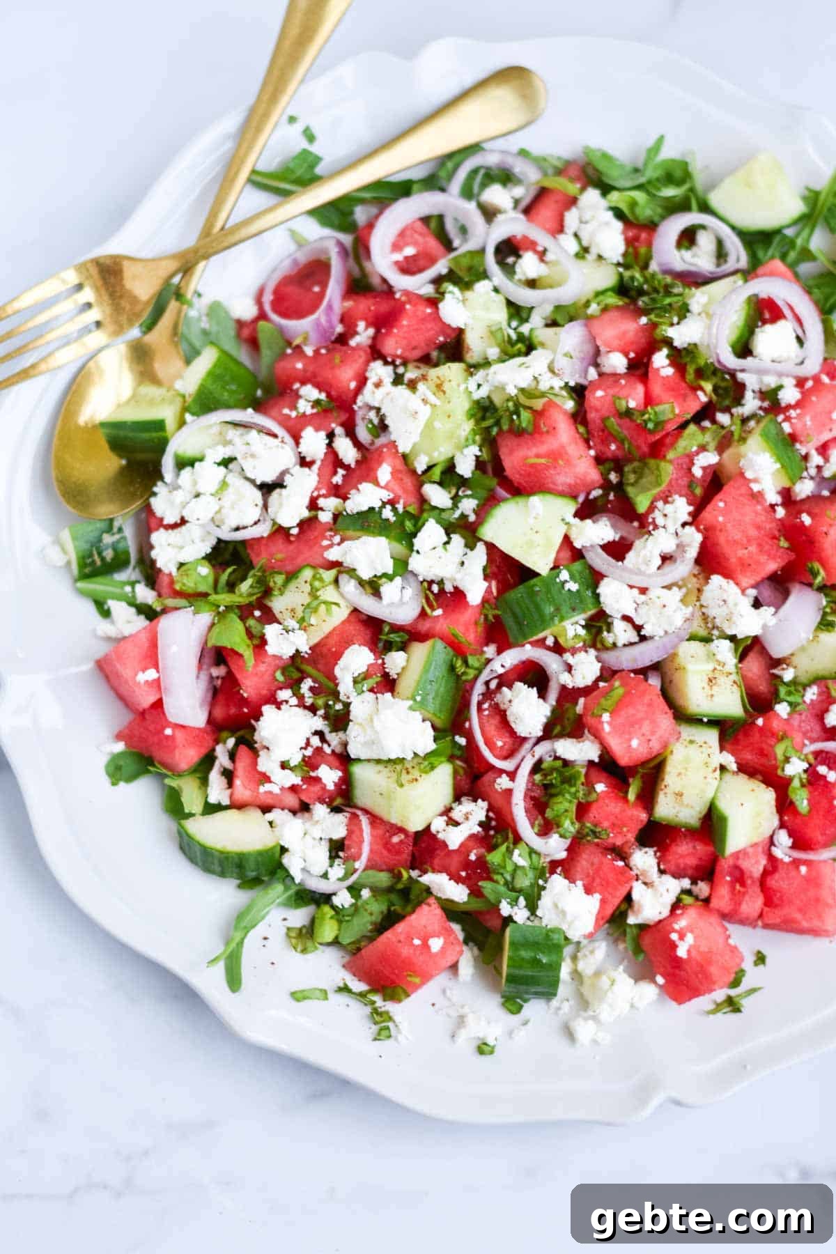 Watermelon salad with gold serving utensils next to it.