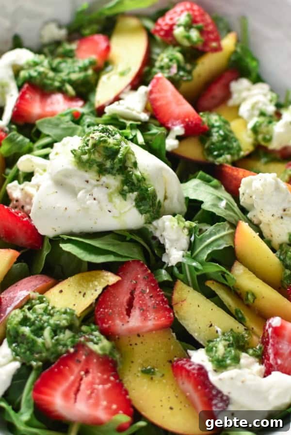 A basil vinaigrette on top of a peach burrata salad in a white bowl.