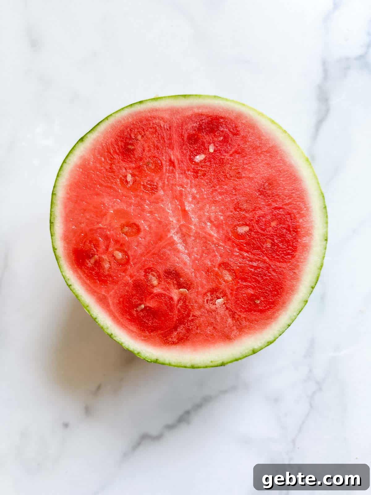 A watermelon sliced in half on a marble table.