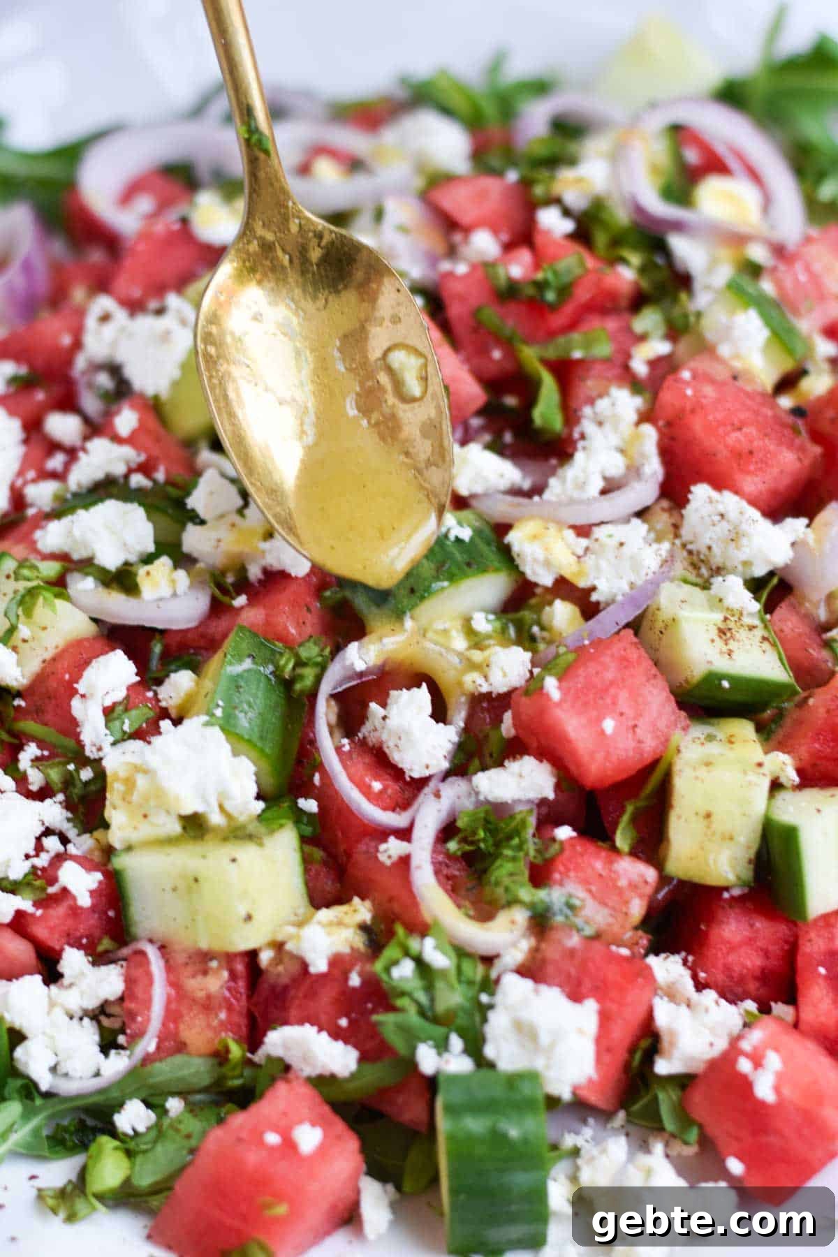 A gold spoon pouring vinaigrette over a watermelon salad.