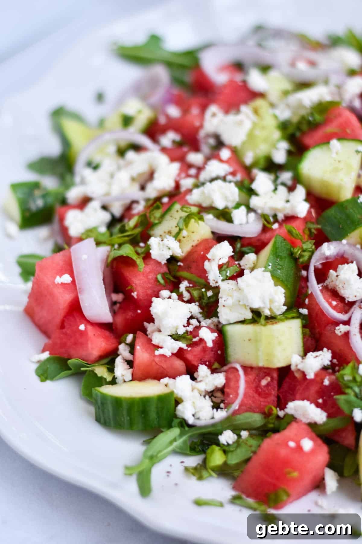 A watermelon basil salad on a white scalloped plate.