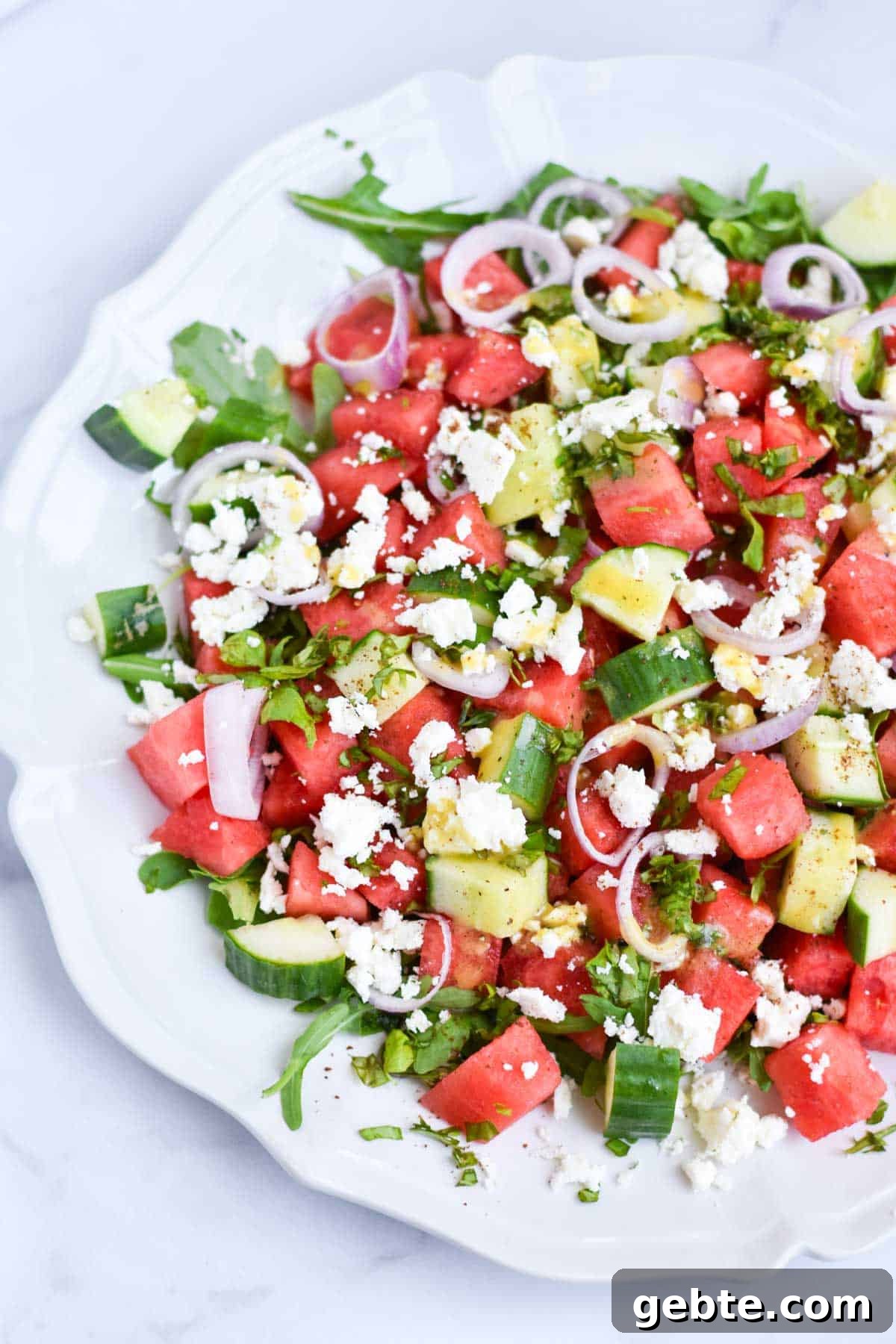 Watermelon salad with arugula on a white scalloped serving plate.