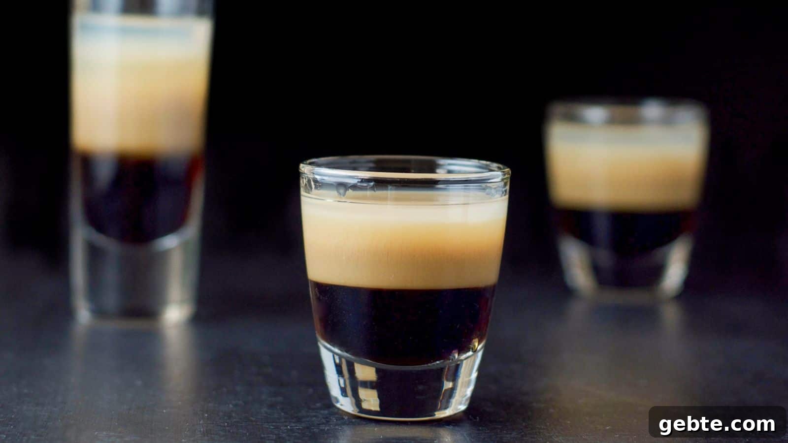 Three glasses layered with a dark, beige and clear liqueur