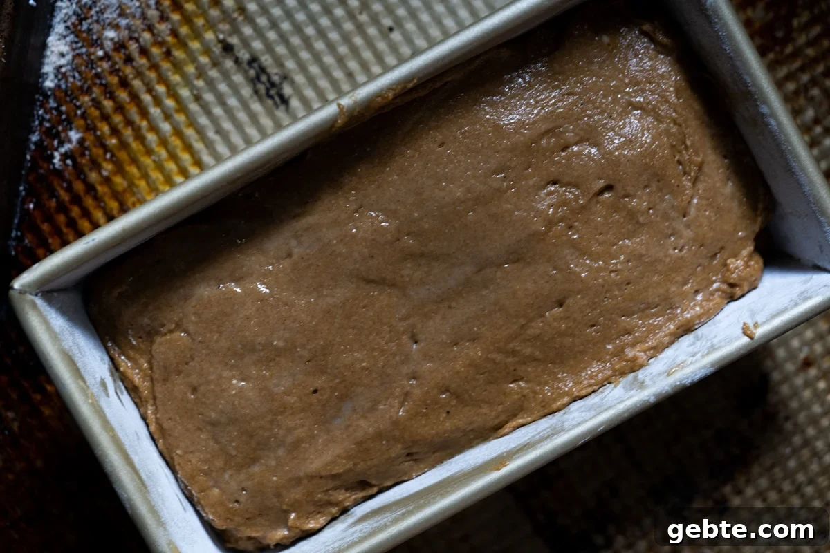 Transferring the almond flour gingerbread batter to a loaf pan and smoothing it out with a wet spatula
