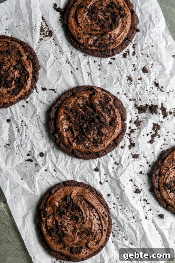 Copycat Crumbl Dirt Cake Cookie Recipe — Soft Chocolate Cake Cookies 4 Chocolate frosted cookies with crushed Oreos on top on parchment paper.