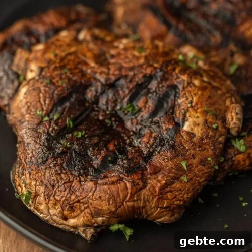 63 Flavorful Grilled Vegetable Recipes for Every Meal 9 Grilled Portobello Mushrooms on a black platter topped with fresh herbs.