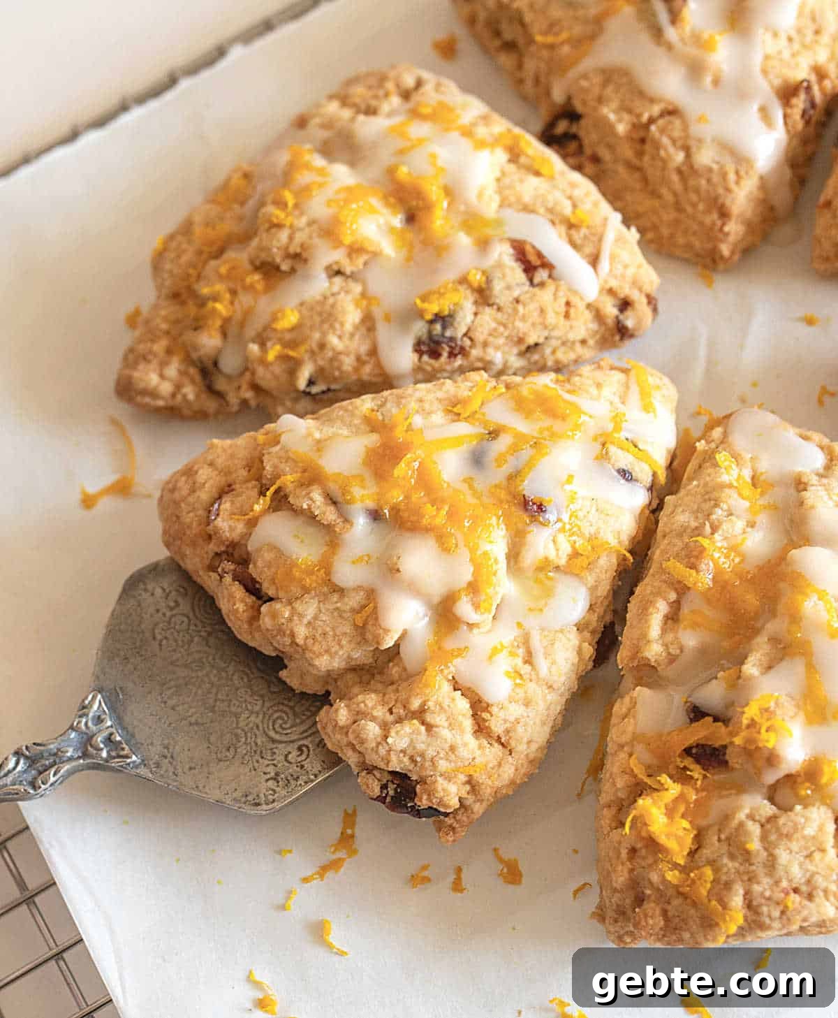 Half circle of glazed orange cranberry scones triangles on parchment paper with a cake server.