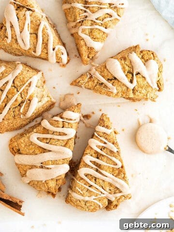 White surface with several triangles of glazed cinnamon scones. Spoon and cinnamon sticks.