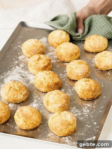 Hand holding metal tray with baked scones and a green cloth.