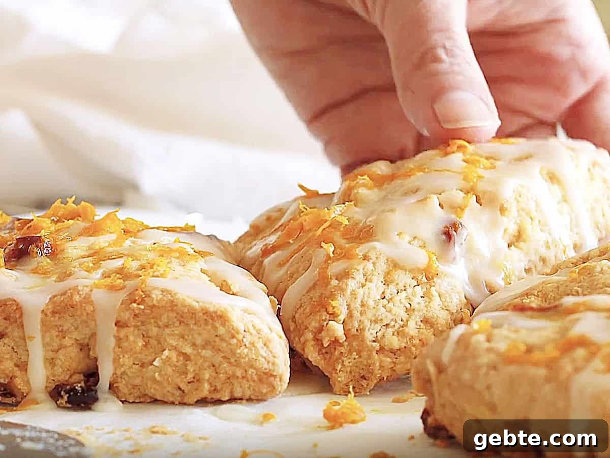 Hand lifting a glazed cranberry orange scone from among others on a white surface.