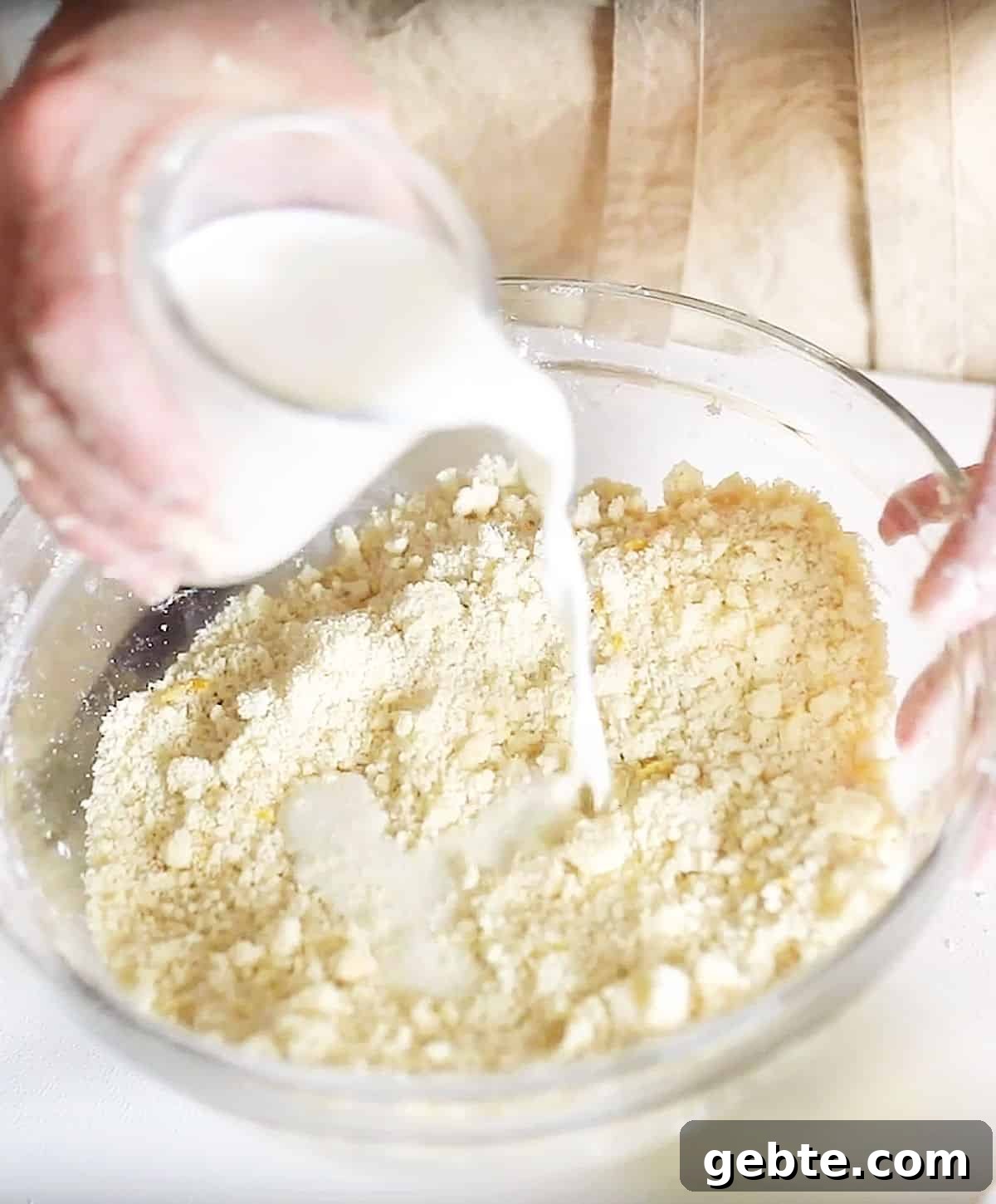 Adding milk to buttery scone dough in a glass bowl.