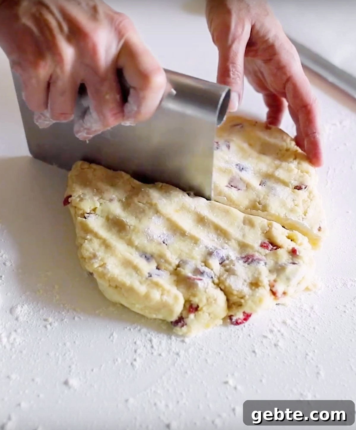 Cutting circle of cranberry scone dough on a white surface with a dough scraper.