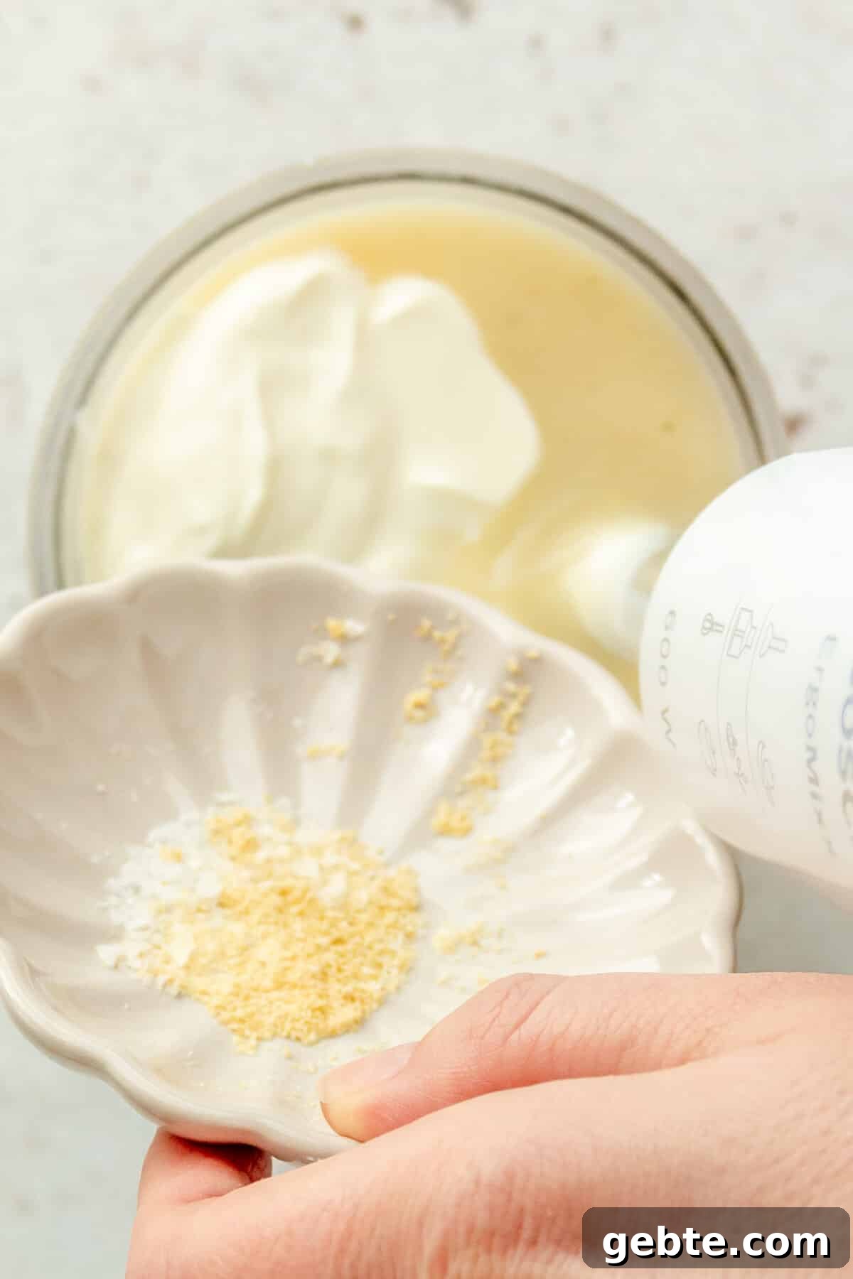 Seasonings are tossed into a blender beaker on a light grey surface.