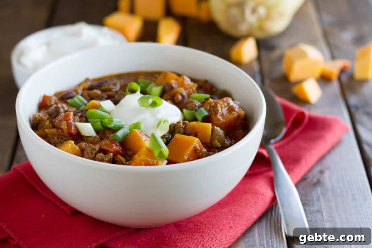 Butternut squash, black beans, and ground beef star in this flavor packed Butternut Squash Chili with Beef. Bowl of butternut squash chili with beef on a red cloth.