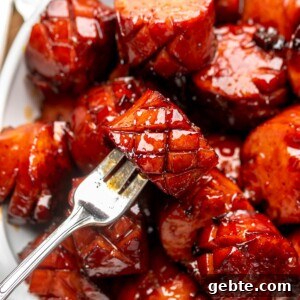Sweet and Spicy Kielbasa Bites — 2-Ingredient Party Appetizer 8 A fork holds a chunk of kielbasa in a bowl of other pieces.