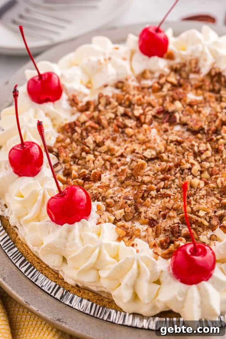 Overhead view of no bake banana split pie topped with chopped pecans, whipped cream, and cherries.