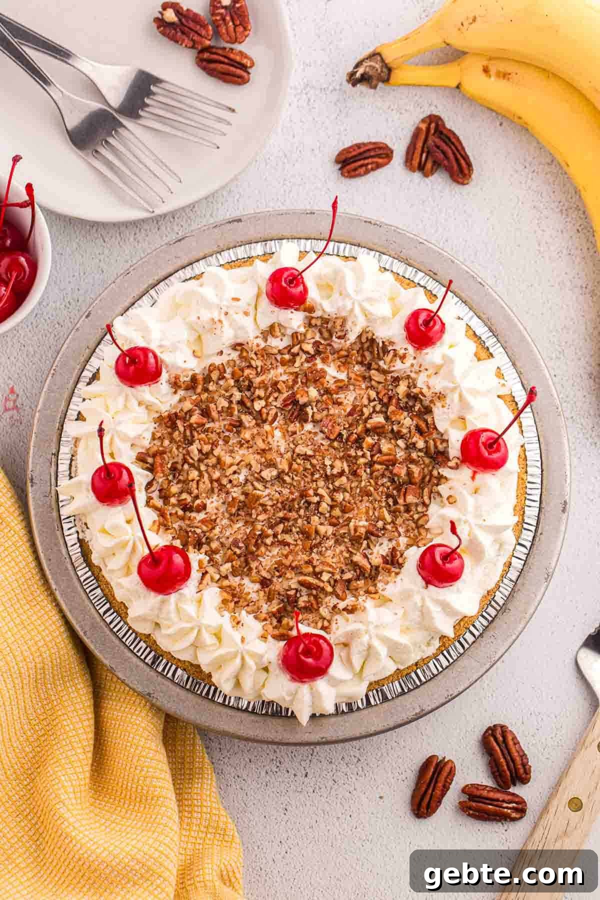 Overhead view of finished no bake banana split pie topped with whipped cream, chopped pecans, and cherries.
