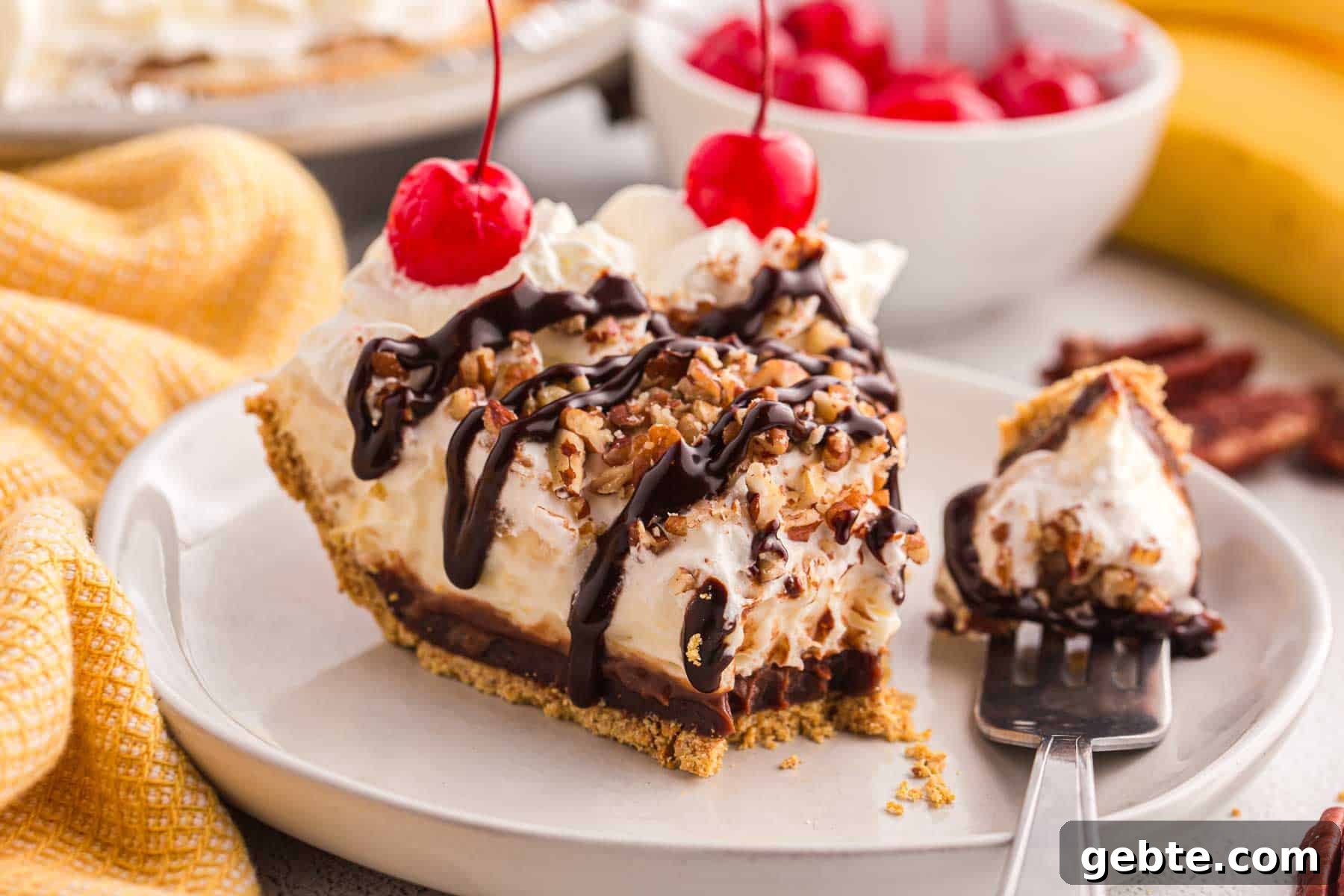Slice of no bake banana split pie topped with whipped cream, chopped pecans, chocolate syrup, and cherries served on a plate with a forkful beside it.