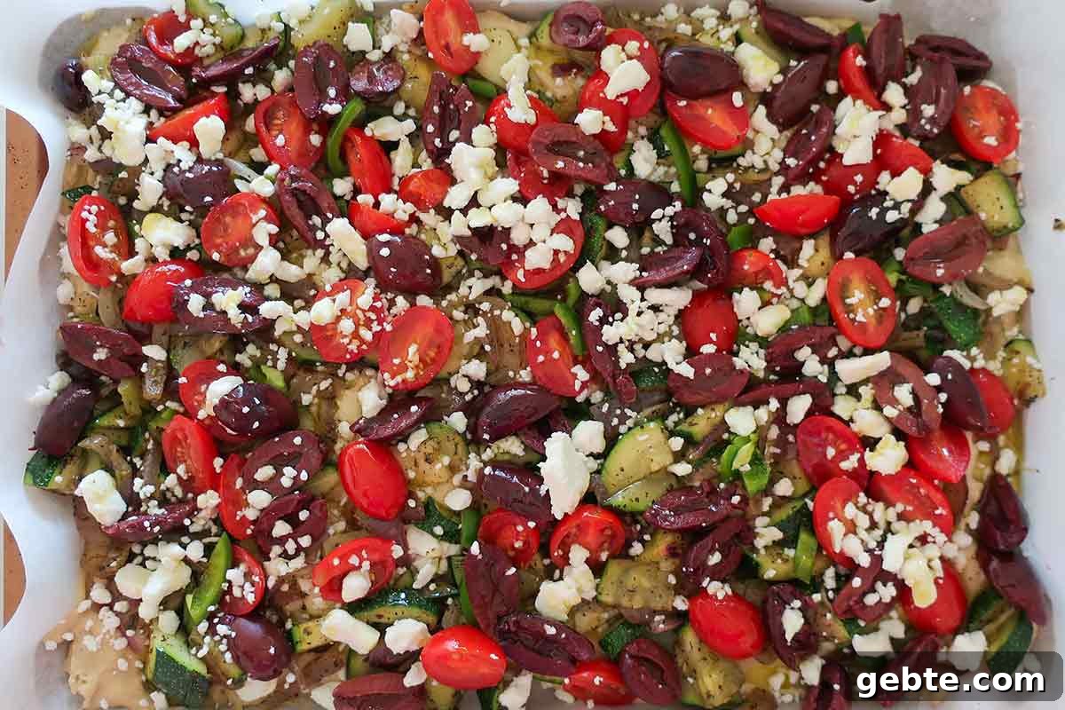 Flatbread-batter-topped-with-veggies-and-feta-in-a-rimmed-baking-sheet-ready-for-the-oven