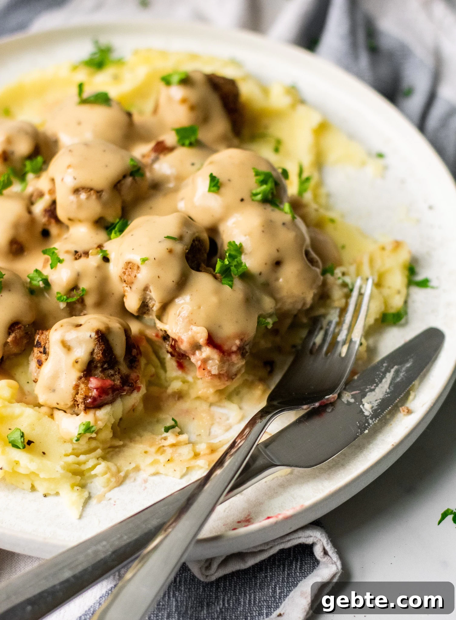 Authentic Swedish Köttbullar Recipe: Classic Meatballs with Creamy Gravy 6 Swedish meatballs with gravy and mashed potatoes on a plate.