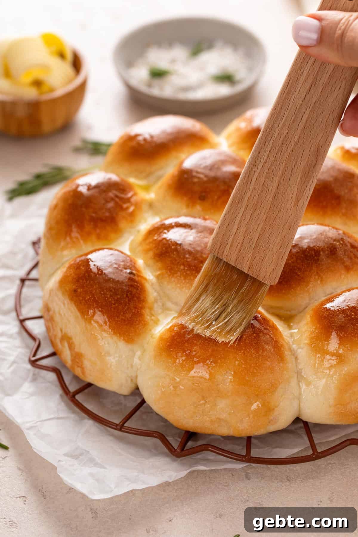Melted butter being brushed on hot brown and serve dinner rolls.