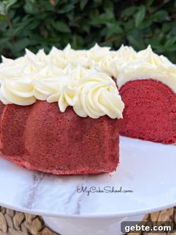 Red velvet pound cake on a white pedestal, topped with cream cheese piping.