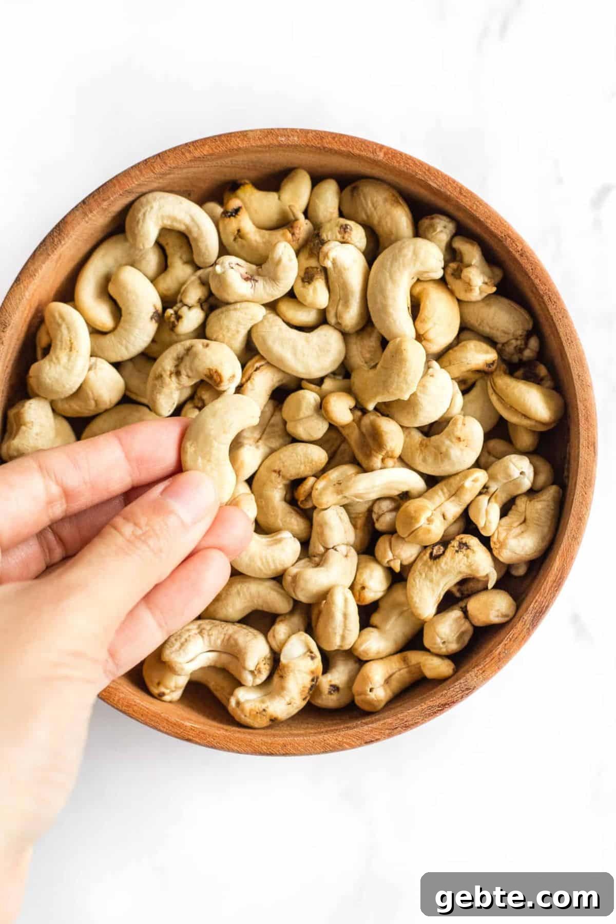Chocolate Cashew Pudding (Gluten-Free, Dairy-Free) Holding up a cashew nut from a bowl of cashews.